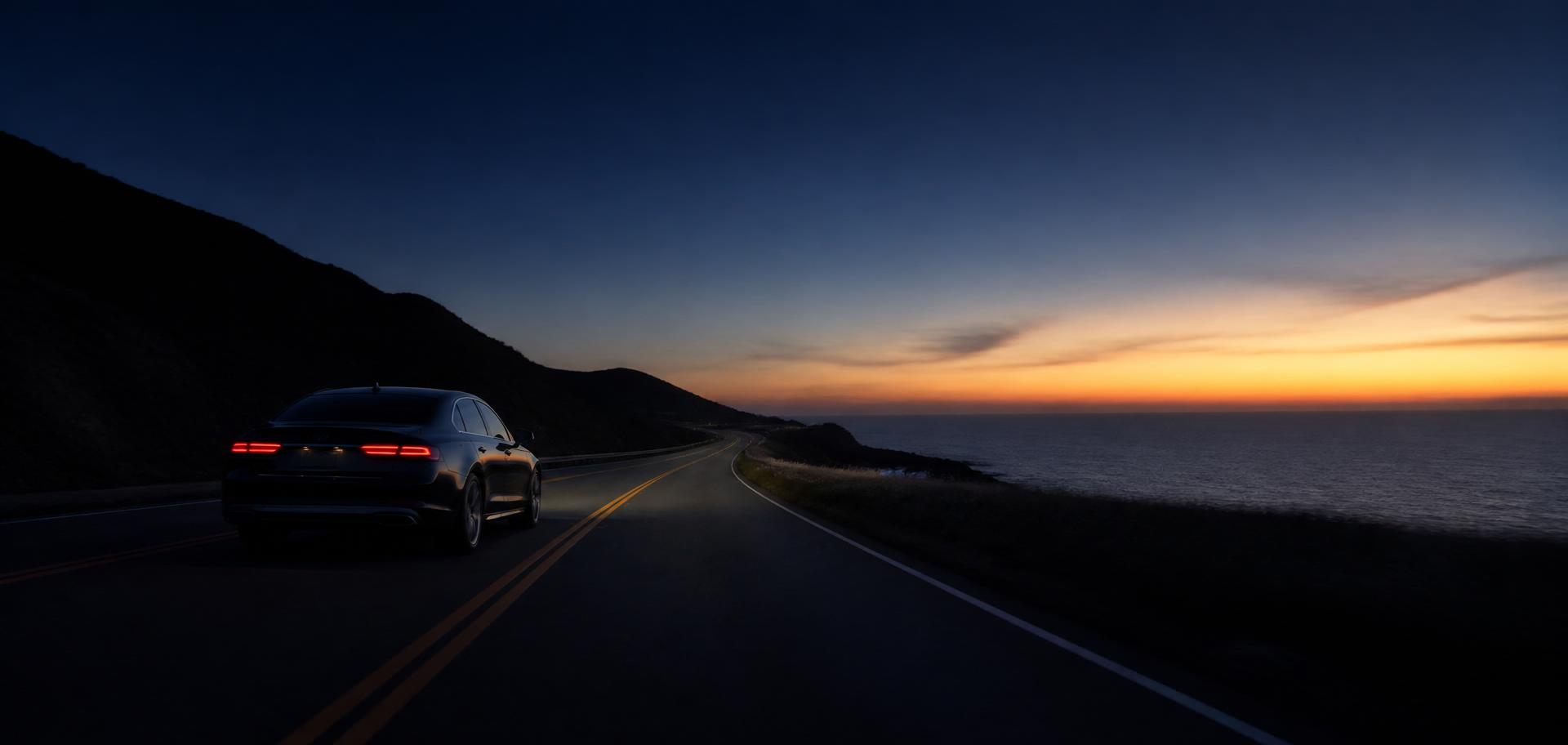 Dark luxury car on a coastal highway at dusk